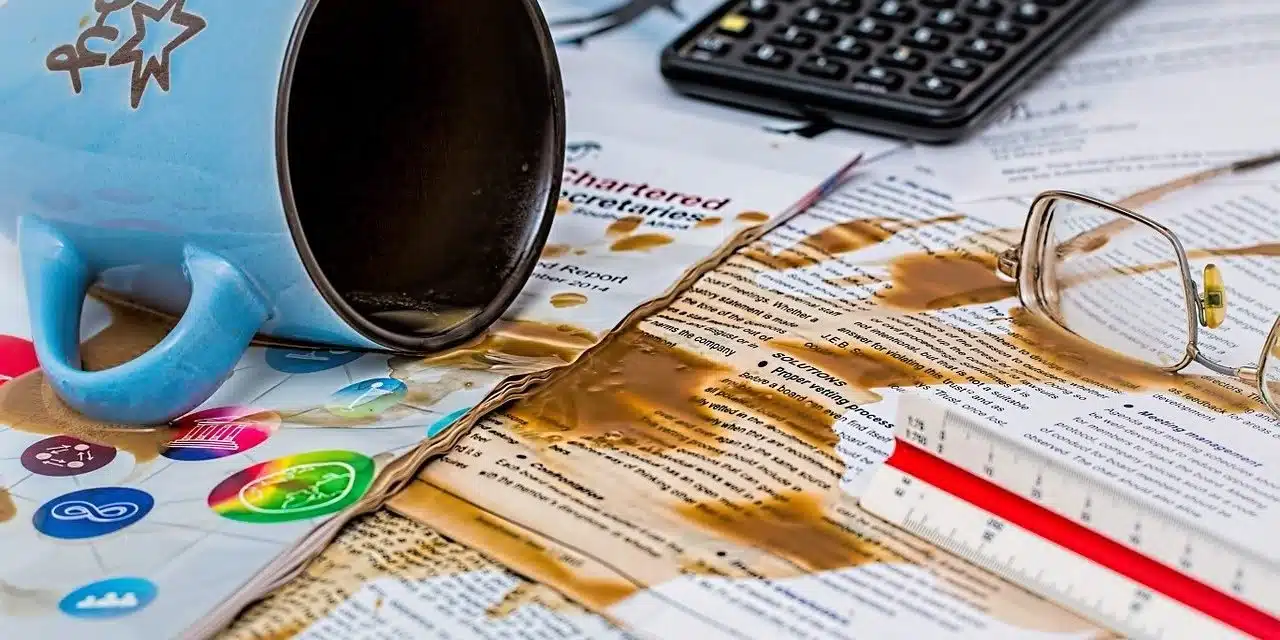 Image of QuickBooks forms spread out, with an overturned coffee cup spilling onto them, illustrating common mistakes that can occur when using QuickBooks and the importance of careful financial management.